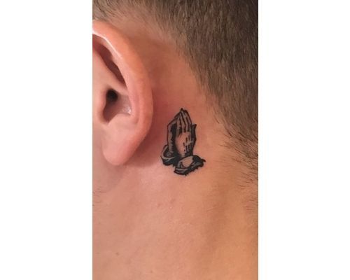 Small praying hands tattoo located behind the ear